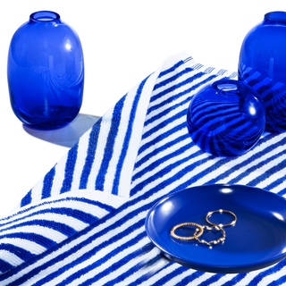 Rings on a blue plate, resting on a striped blue and white towel, next to blue transparent vessels