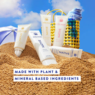 Several Native Mineral Suncare tubes in sand with a beach bag and umbrella in the background